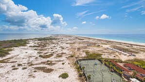 An aerial view of a coastal area with a beach, a tennis court, and a building with a red roof. - Stunning Coastline Views at Portofino 2-1503! (Pensacola Beach)