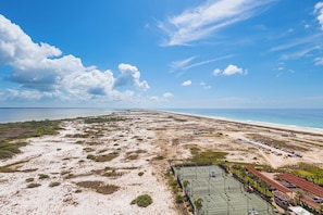 Luftaufnahme einer Küstenlandschaft mit Strand, Tennisplatz und einem Gebäude mit rotem Dach.
