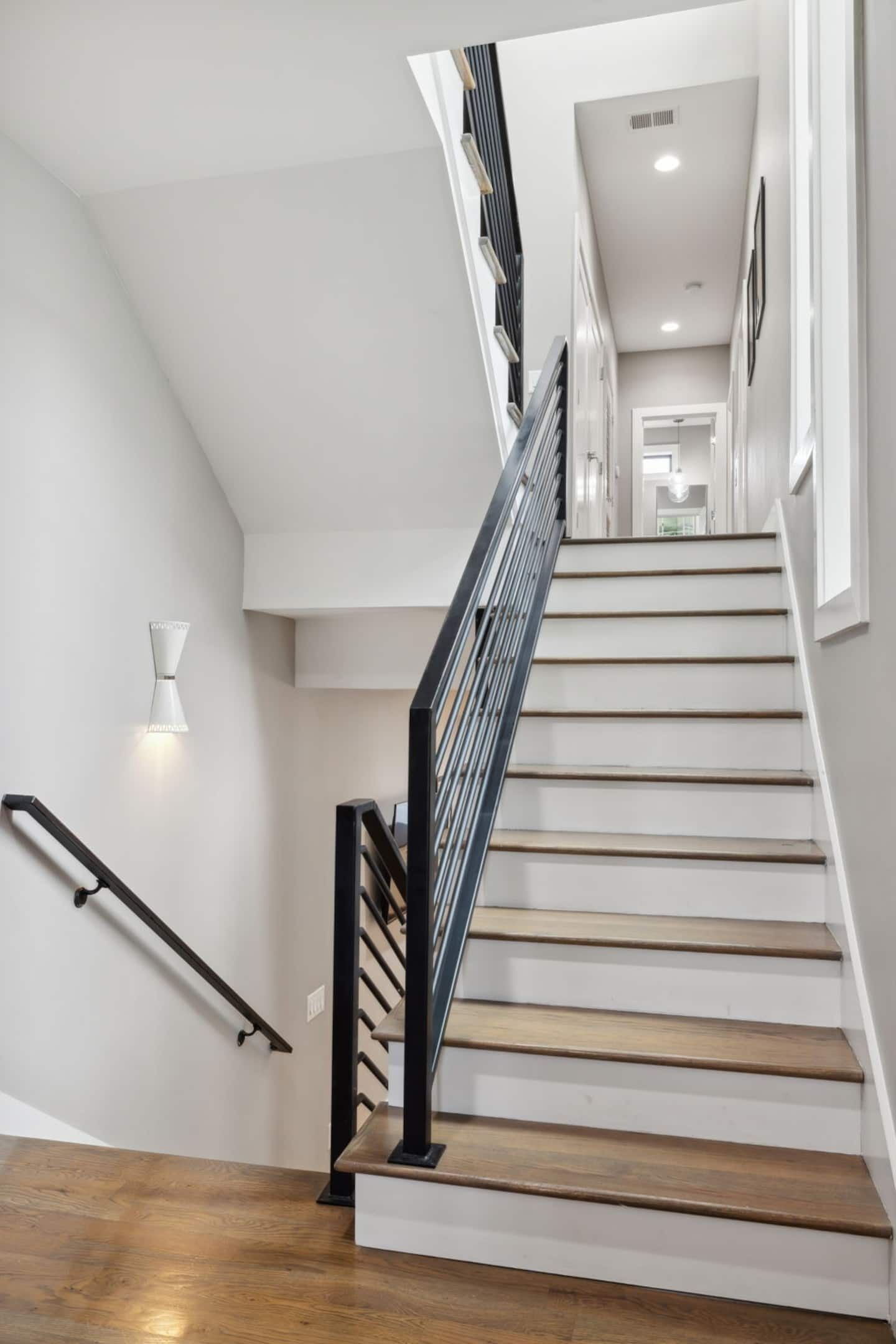 A staircase with wooden steps and a black handrail, leading to a landing with a light fixture.