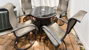 Eine Terrasse mit einem runden Tisch und sechs Stühlen, umgeben von einem weißen Zaun, unter einem Baum.