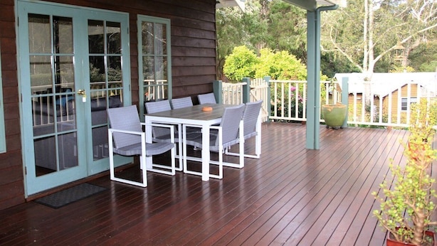 A wooden deck with a table and chairs, a covered patio area, and a view of a forested area.