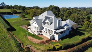 A large house with a prominent 'Z' on the roof, surrounded by a well-maintained lawn and a tennis court. - Expansive Hamptons home on acreage, with pool, spa, gym, tennis court & views. (Kangaloon)