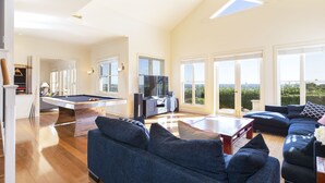 A spacious living area with a pool table, a sofa set, and a kitchen area with a TV. - Expansive Hamptons home on acreage, with pool, spa, gym, tennis court & views. (Kangaloon)