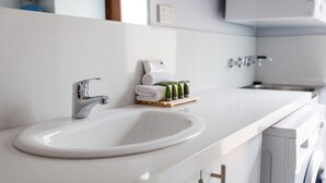 Ein modernes Badezimmer mit einem weißen Waschbecken, einem Chromarmaturen und einem kleinen Ablagefach mit Toilettenartikeln.