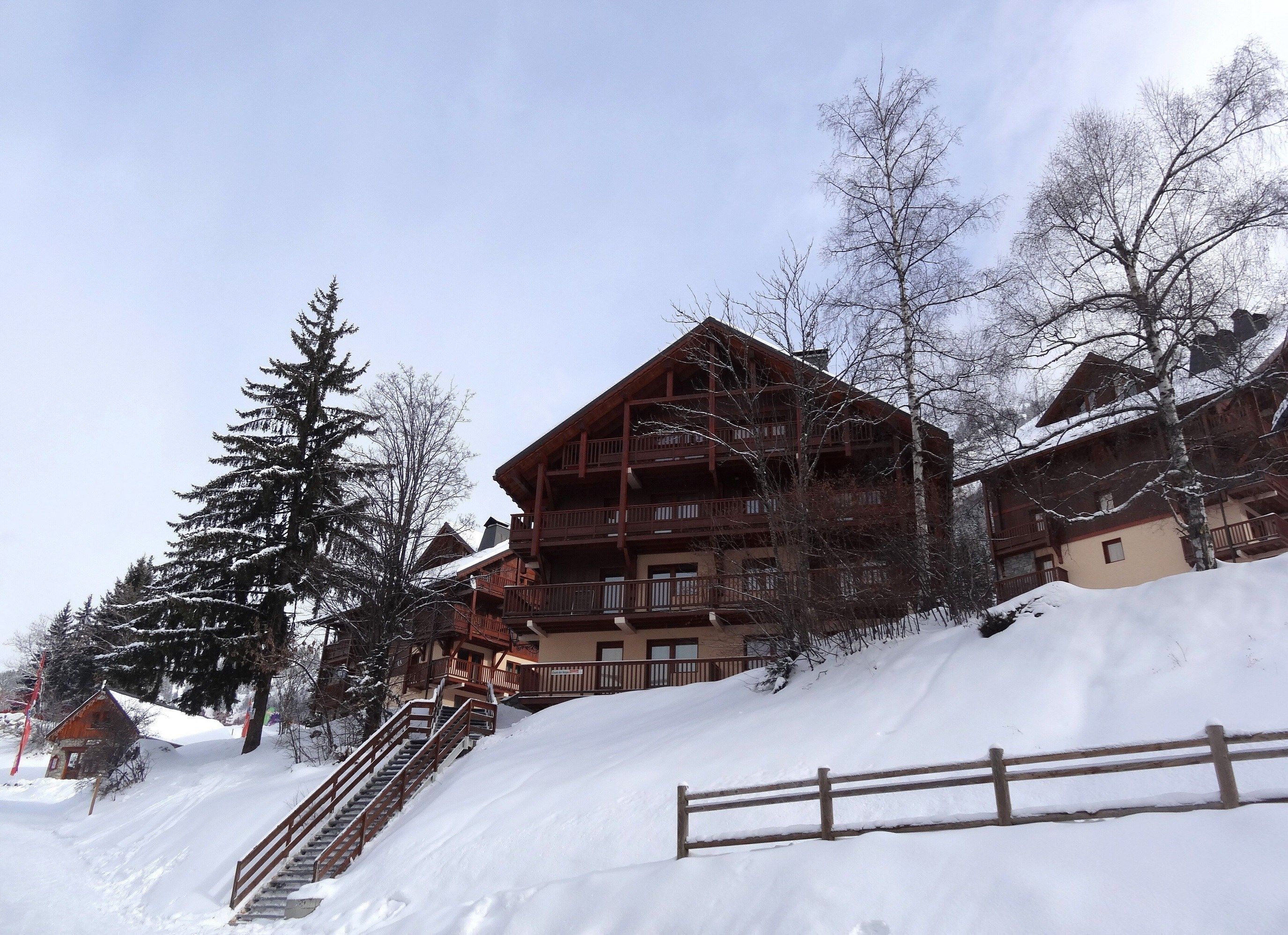 A multi-story wooden lodge with balconies, surrounded by snow-covered trees and a wooden fence.