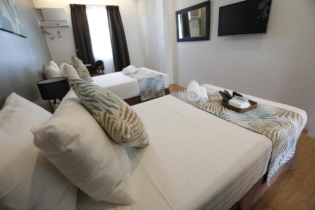 A hotel room with two beds, a desk, a chair, a TV, and a mirror.