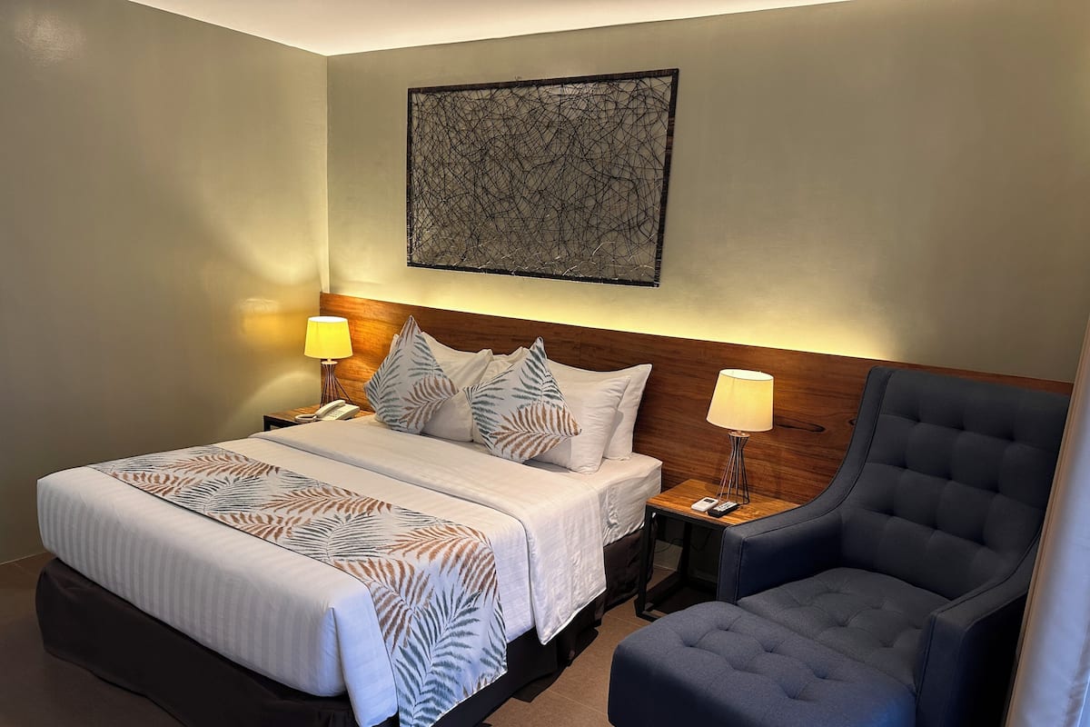 A hotel room with a large bed, two bedside tables with lamps, a chair, and a decorative wall piece.