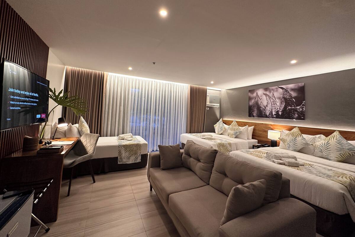 A modern hotel room with a large bed, a sofa, a TV, and a desk.