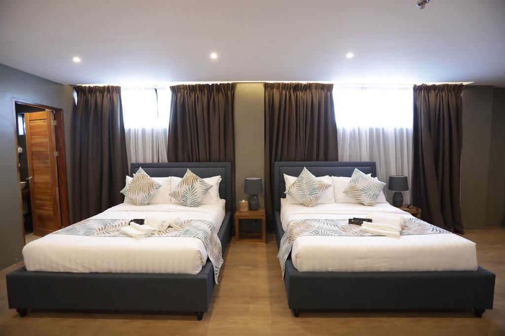 A double bed room with two bedside tables, a lamp, and a window with curtains.