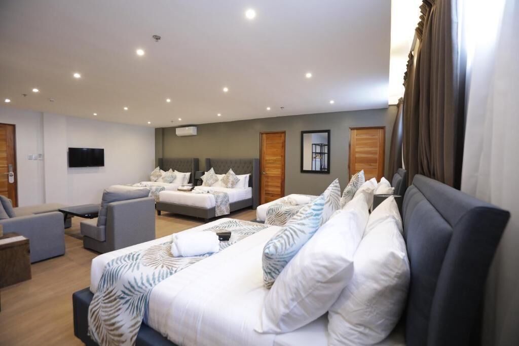 Quarto de hotel com uma cama grande, duas camas menores, um sofá e uma televisão.