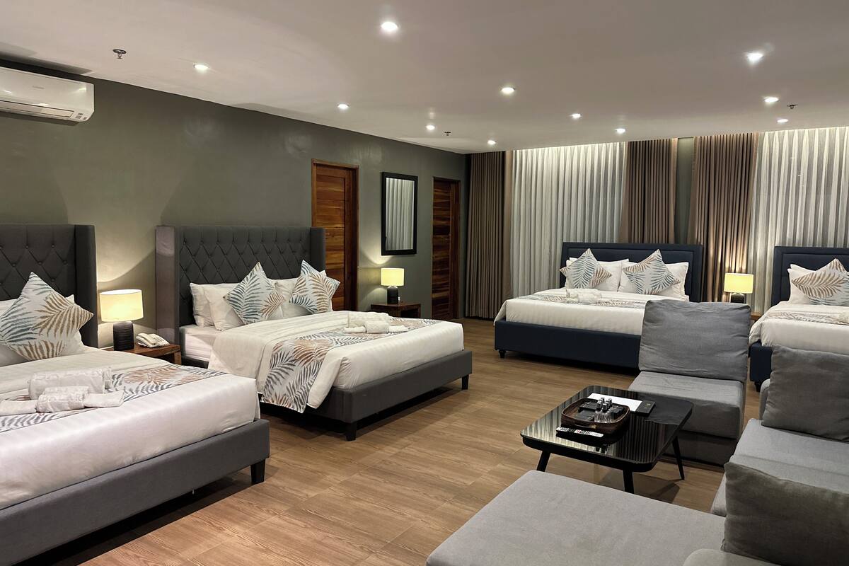 A hotel room with two beds, a sofa, a coffee table, and a wall-mounted air conditioner.