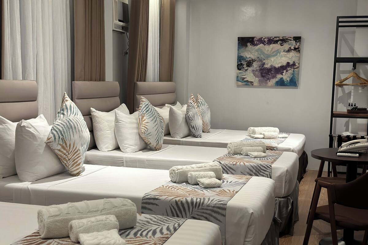 A hotel room with two beds, each with white bedding and patterned pillows, a small table with a phone, and a painting on the wall.