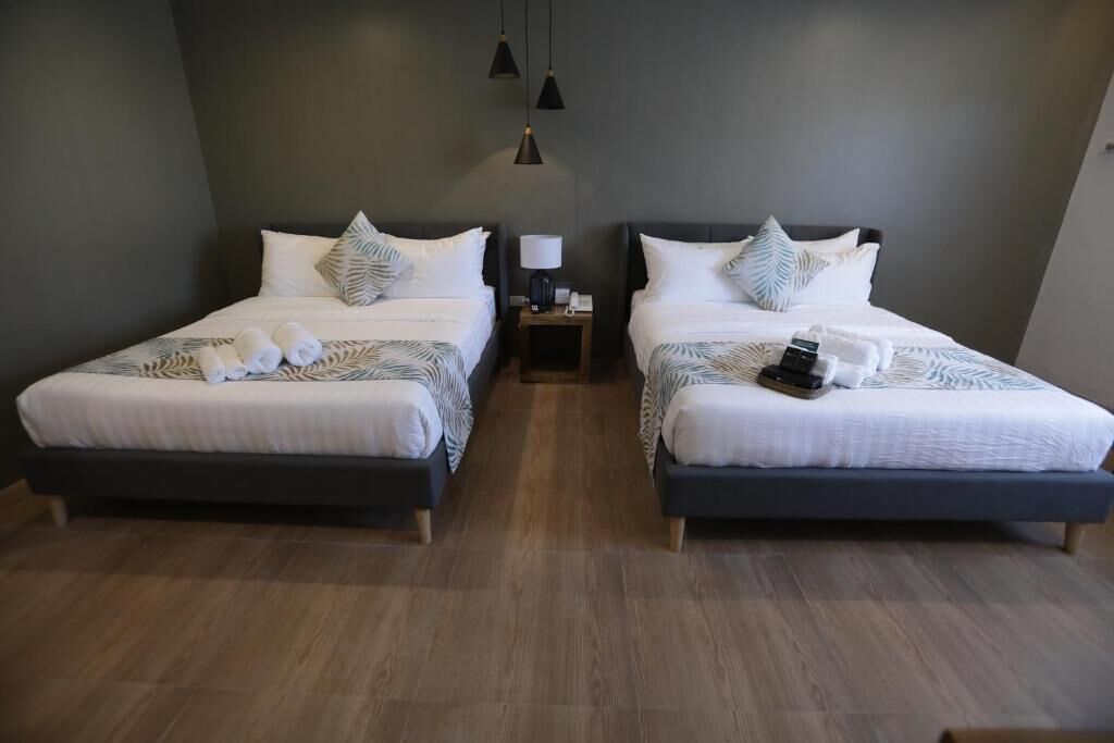 A hotel room with two beds, each with a nightstand, a lamp, and towels.