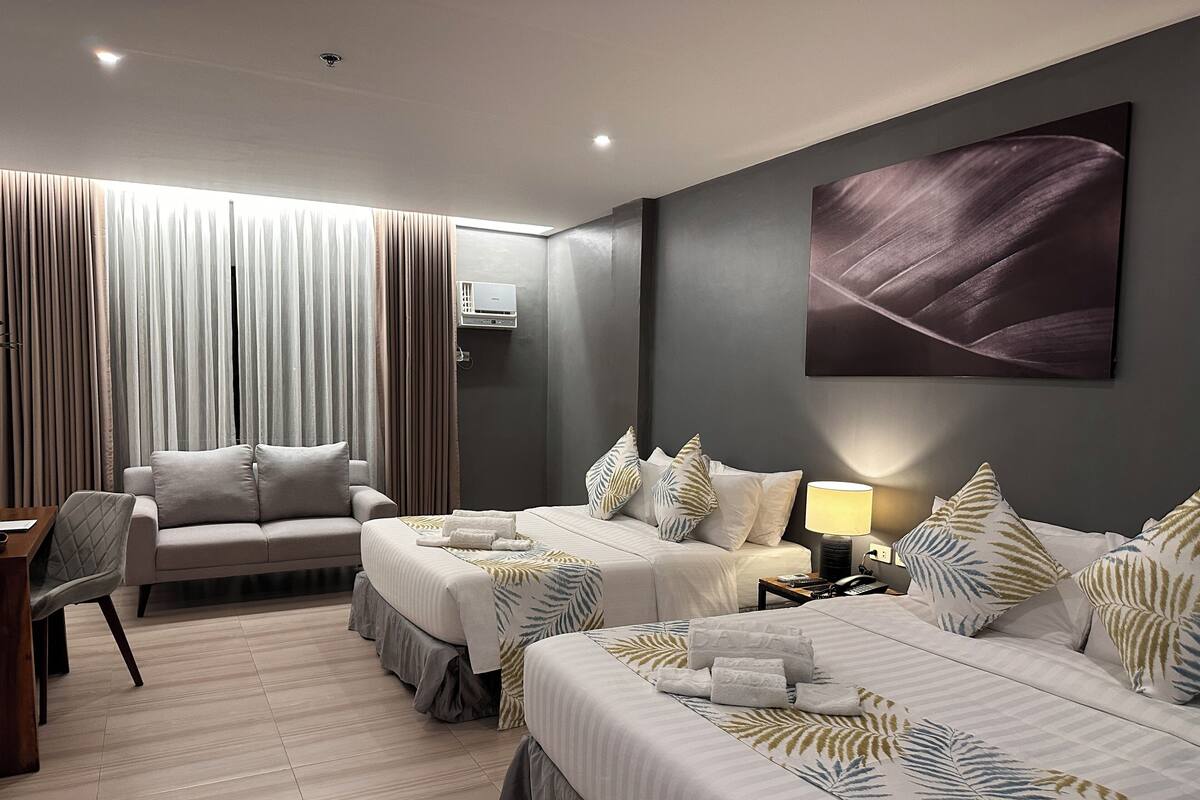 A modern hotel room with two beds, a sofa, a desk, and a large window with curtains.