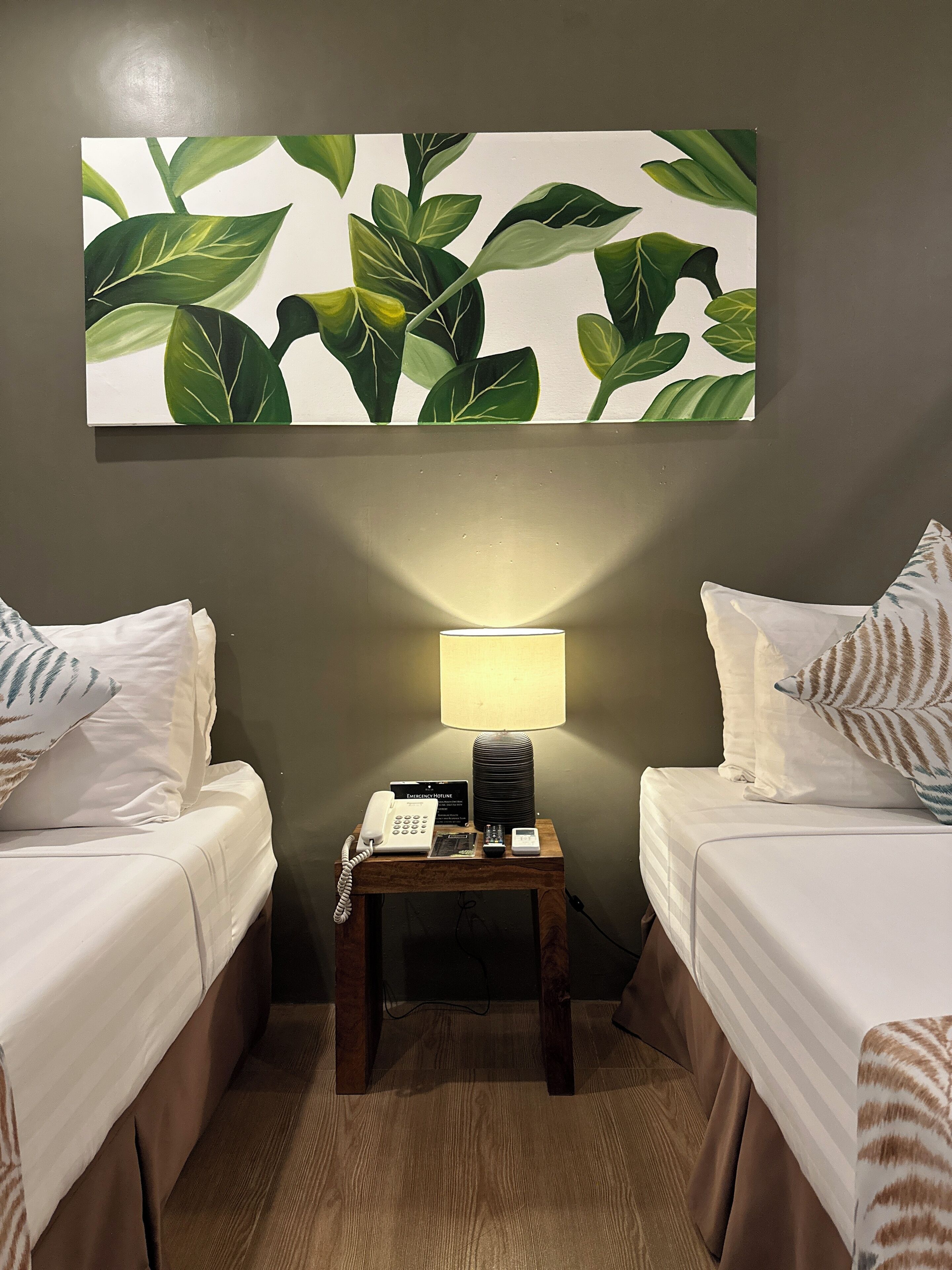 Et hotelværelse med to senge, et sengebord med lampe, en telefon og et skilt, der angiver en nødtelefon.