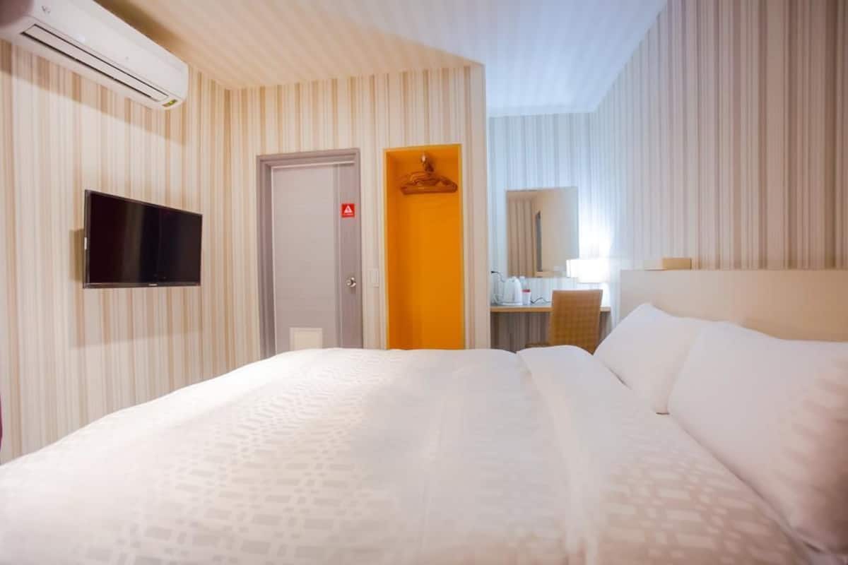 A hotel room with a bed, a television, a mirror, and a bathroom door.