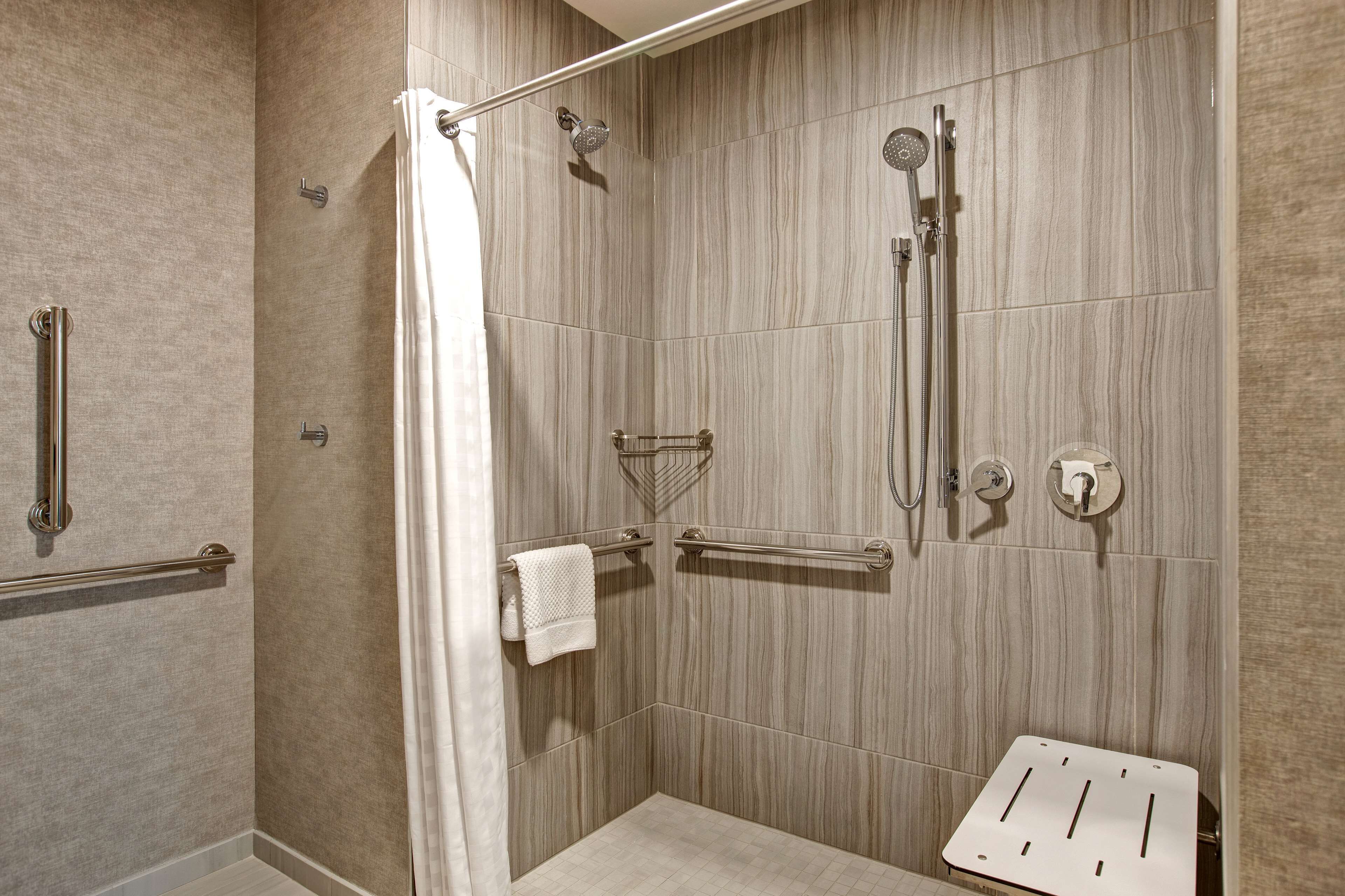 A walk-in shower with a glass door, a handrail, a towel rack, and a shower control panel.