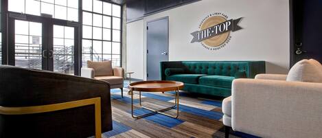 Un área de descanso moderna con un sofá verde, una mesa de centro redonda y un sillón oscuro. Un letrero en la pared dice 'THE TOP' con un logo.