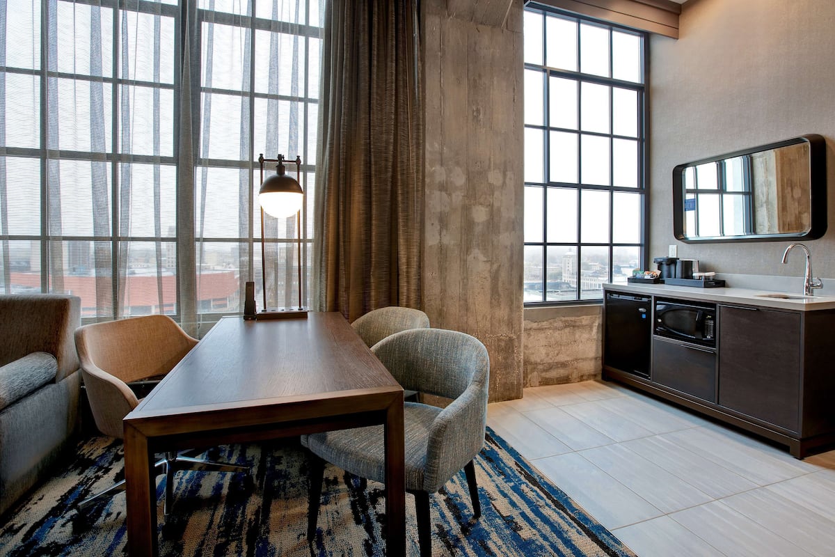 Una habitación de hotel moderna con zona de comedor, un ventanal con vistas, cocina y un espejo grande.