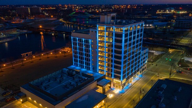 A modern building with a glass facade, adjacent parking area, and a river in the background. - Embassy Suites by Hilton Rockford Riverfront (Rockford)