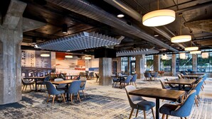 A modern dining area with tables and chairs, large windows, and a patterned carpet. - Embassy Suites by Hilton Rockford Riverfront (Rockford)
