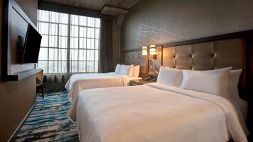 Quarto de hotel com duas camas, televisão de tela plana, escrivaninha e uma janela grande.