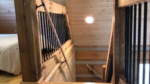 Una escalera de madera con barandilla y vista a un dormitorio con cama y mesita de noche.