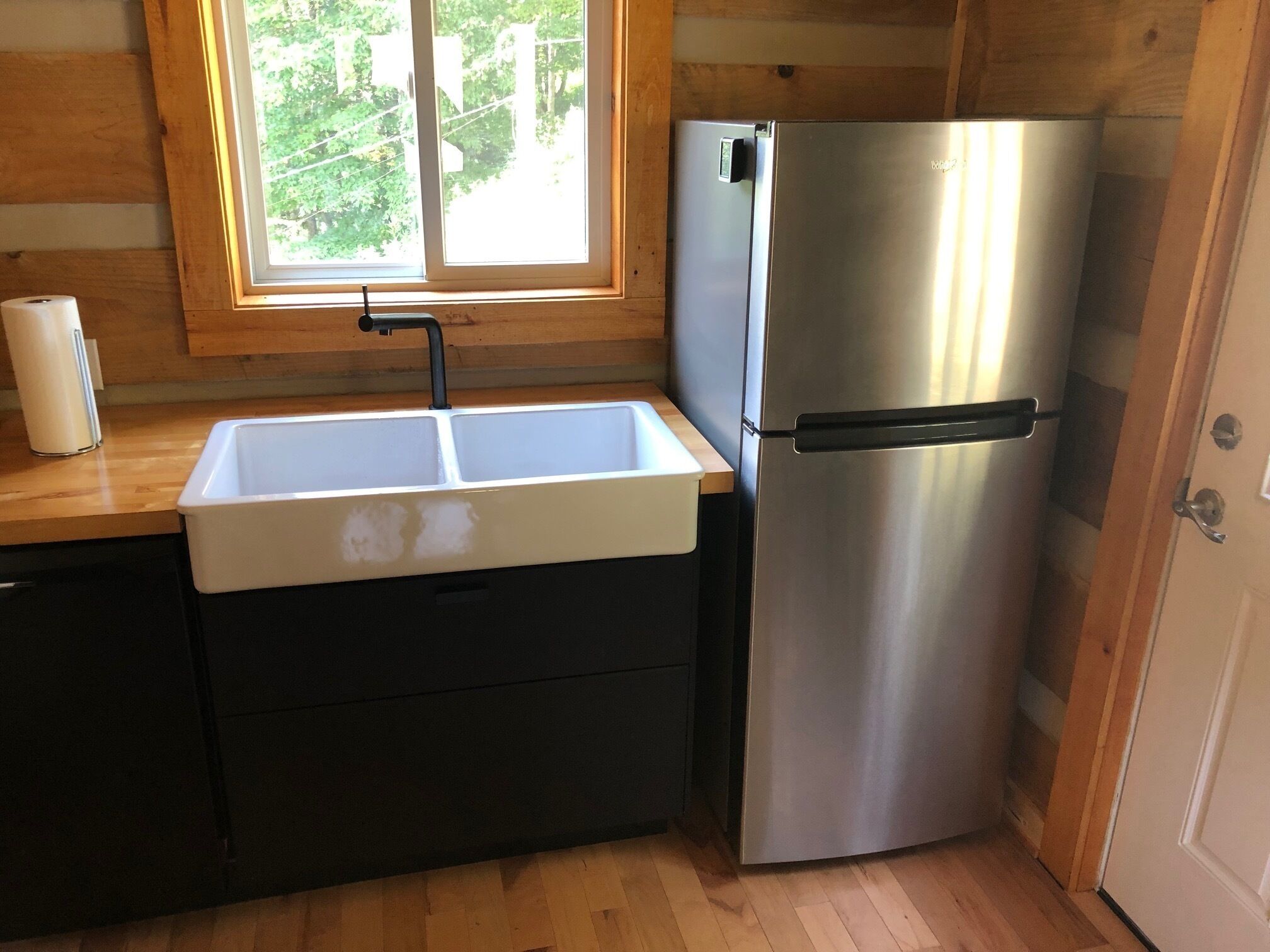A compact kitchen with a stainless steel refrigerator, a white sink, and wooden cabinetry.