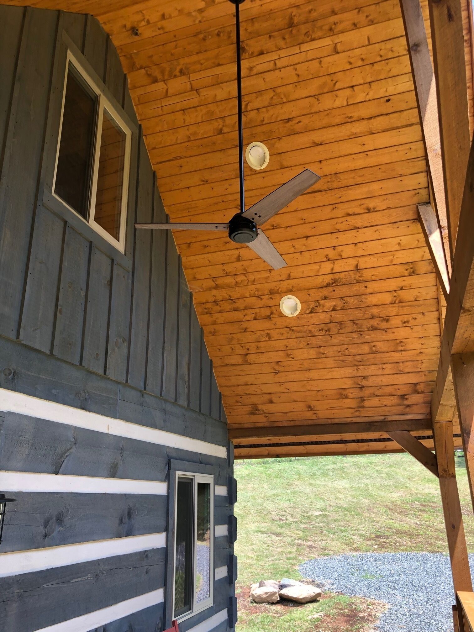 A cabin with a sloped wooden roof, a ceiling fan, and a window with a view of the surrounding landscape.