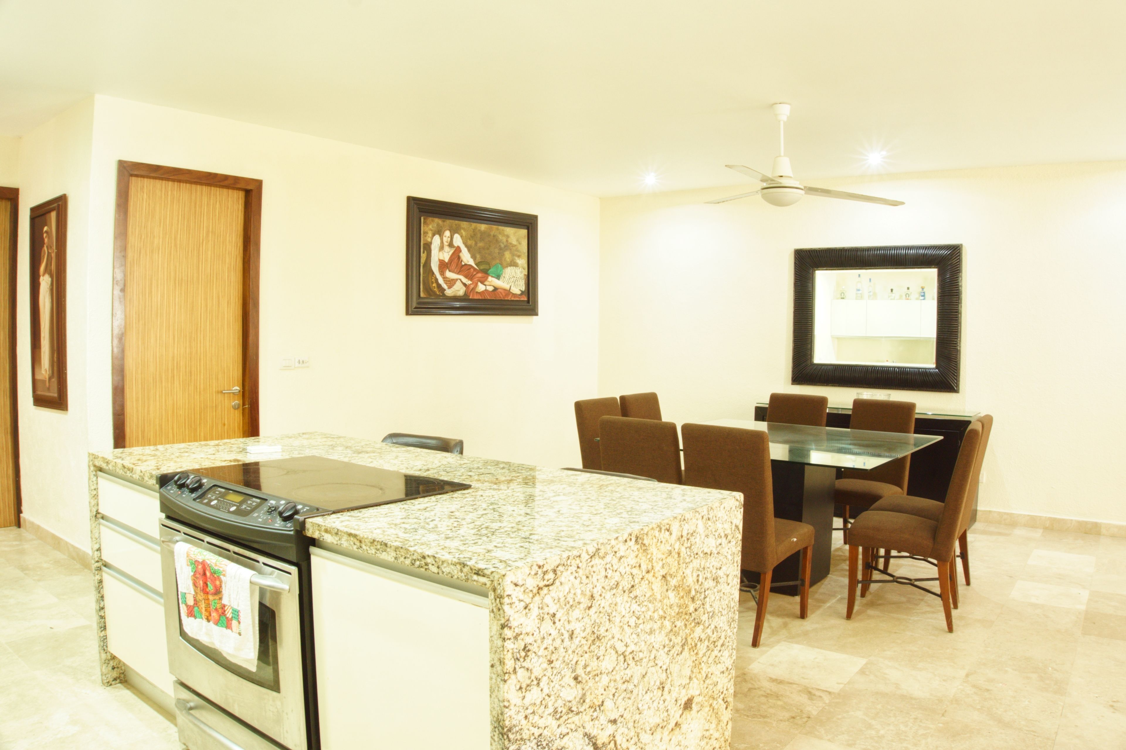 Una cocina con encimera de granito, estufa y comedor con mesa de vidrio y sillas marrones.