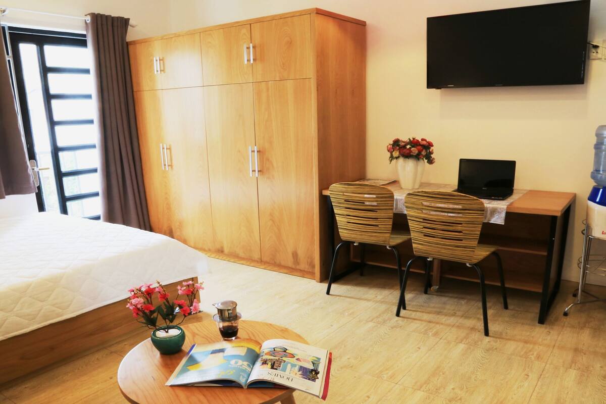 A hotel room with a bed, a desk with a laptop, a water dispenser, and a TV on the wall.