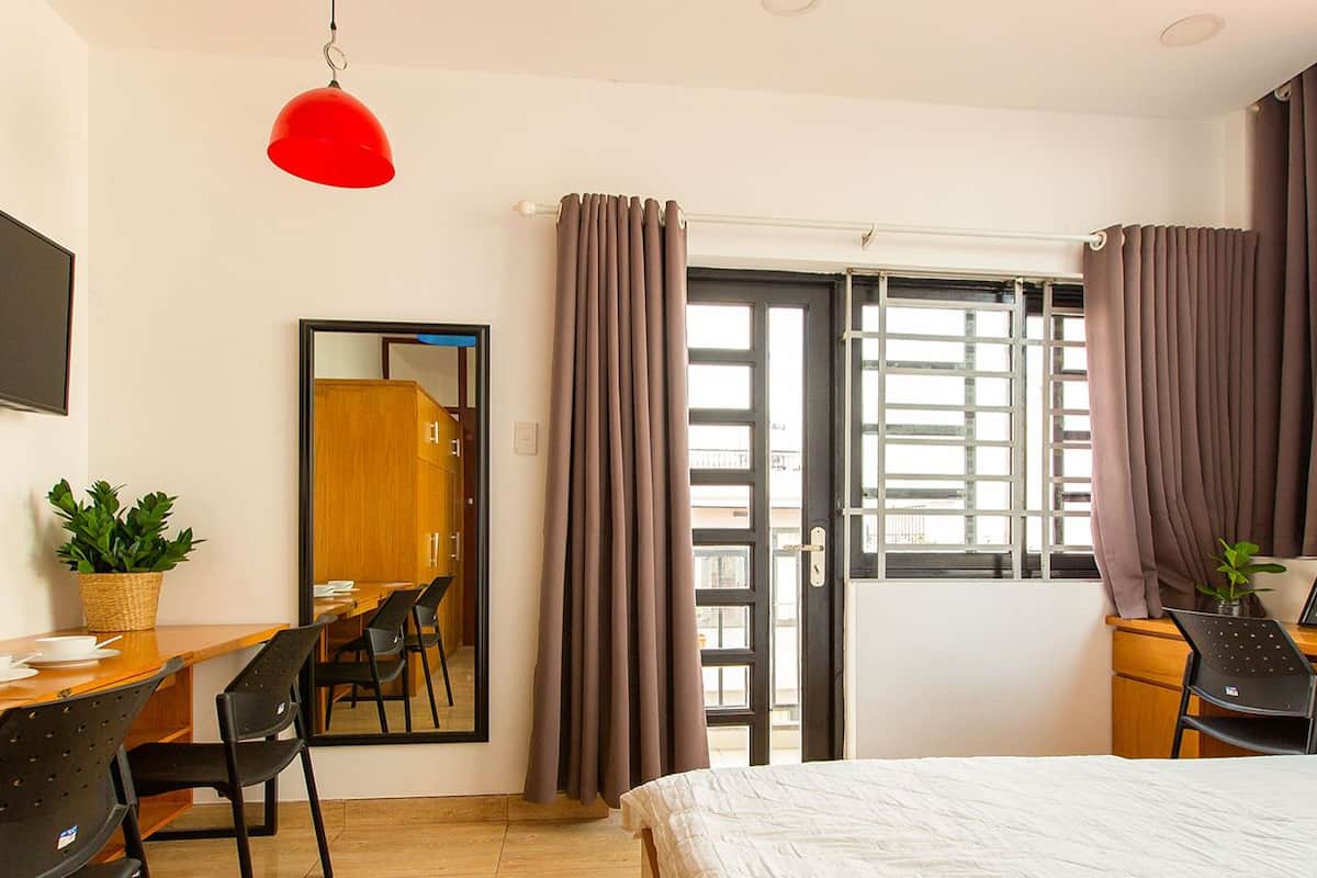 A hotel room with a bed, desk, chairs, a TV, a mirror, and a window with curtains.