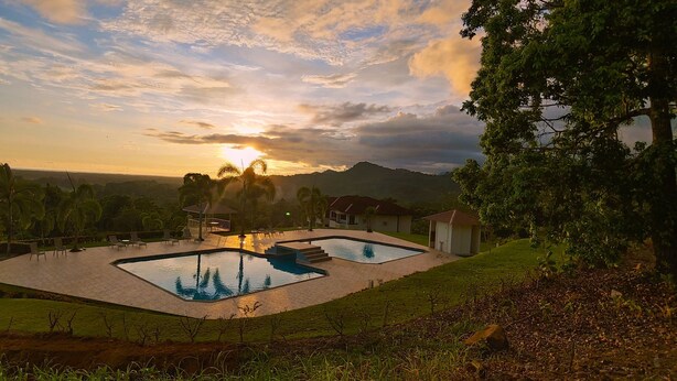 A pool area with a gazebo, surrounded by palm trees and a view of distant mountains.