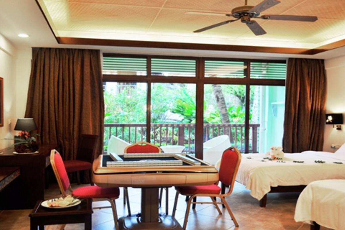 Habitación de hotel con una mesa de comedor, dos camas, un televisor y ventanas grandes con cortinas.