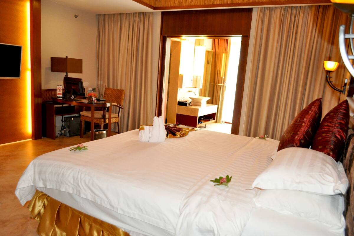 Habitación de hotel con una cama grande, un escritorio, una silla y un baño visible a través de una puerta abierta.