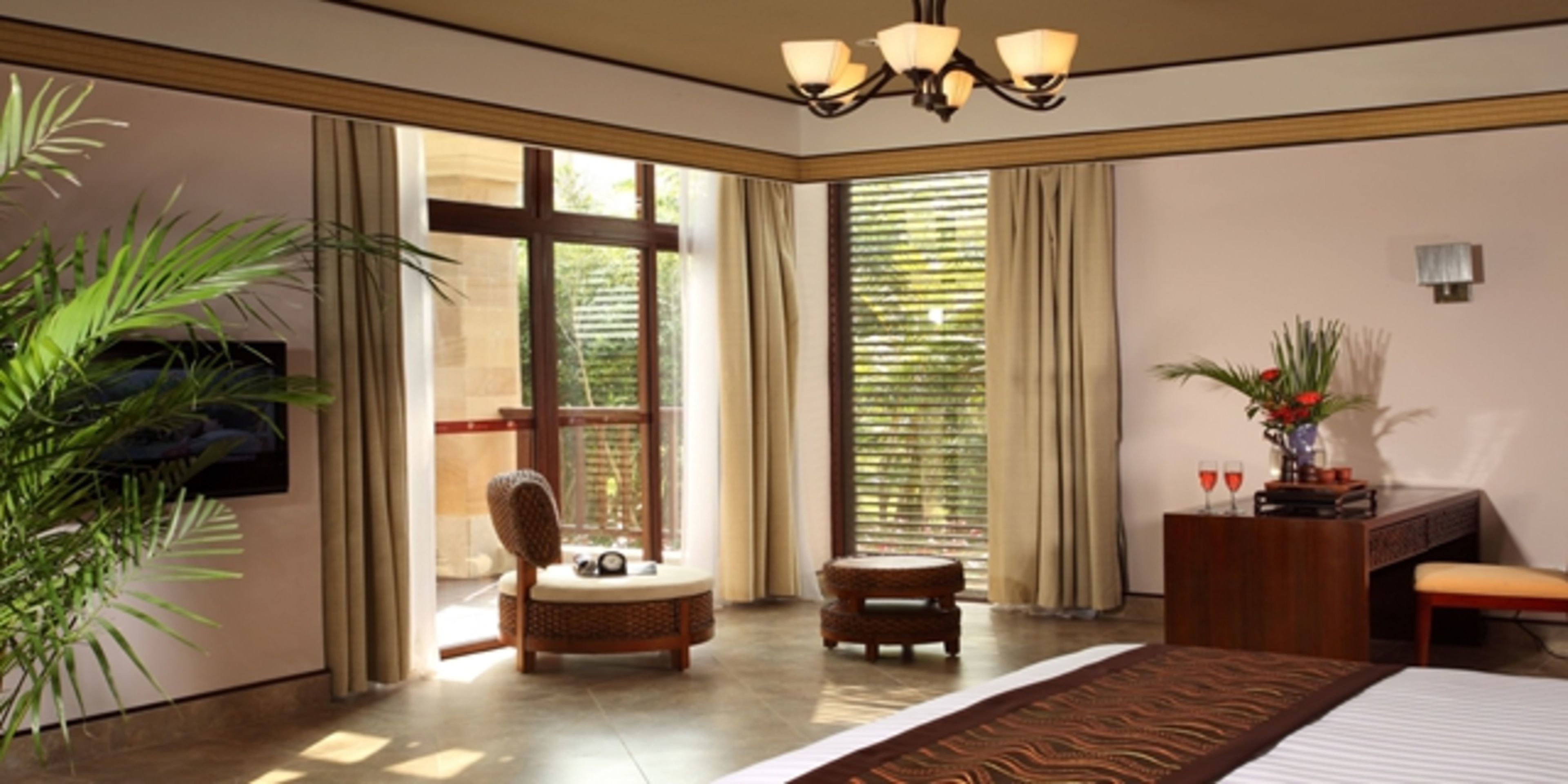 A hotel room with a bed, a desk, a chair, a small table, and a large window with curtains.