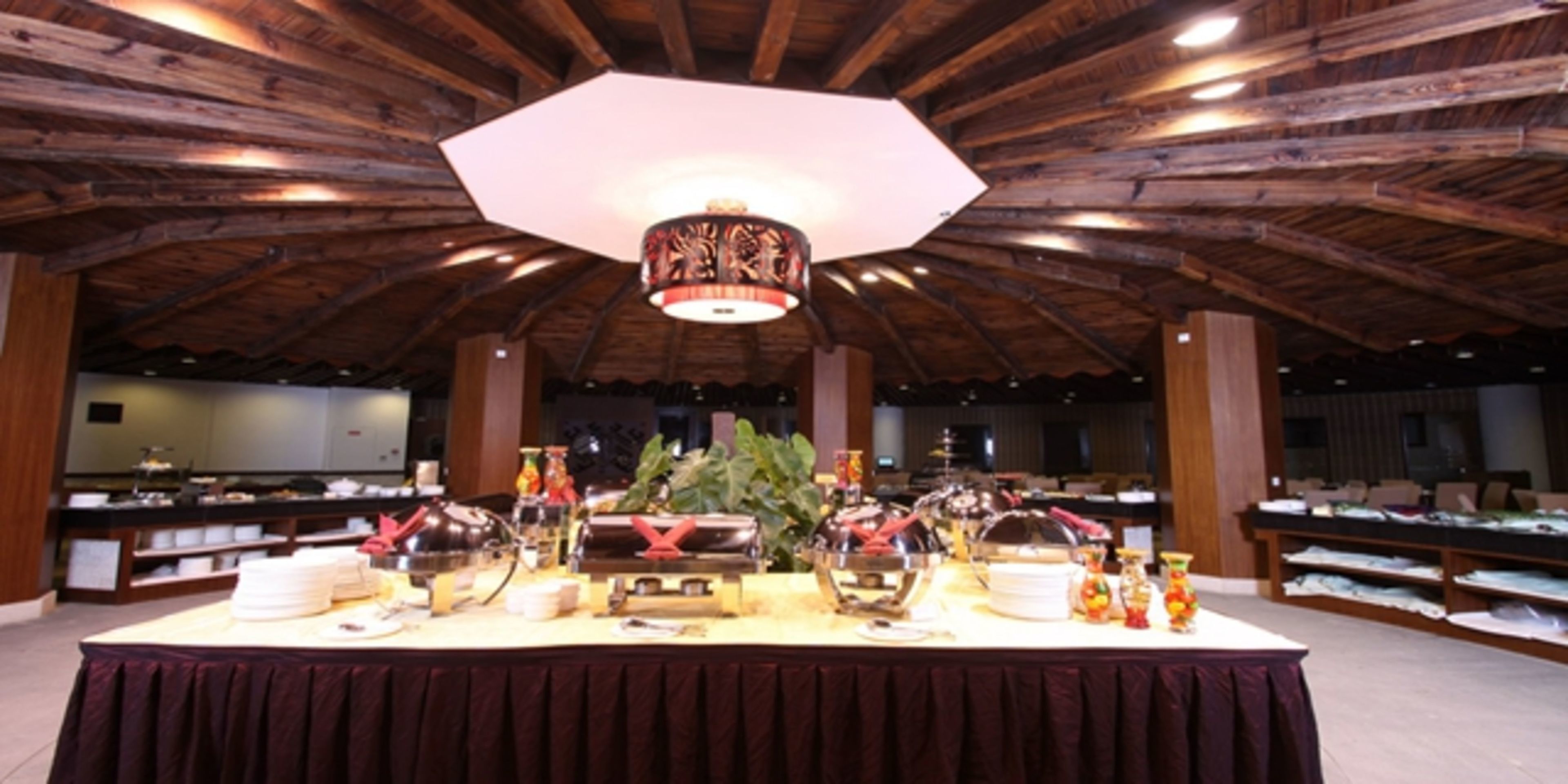 A buffet setup with multiple serving stations, a large central chandelier, and a wooden ceiling structure.