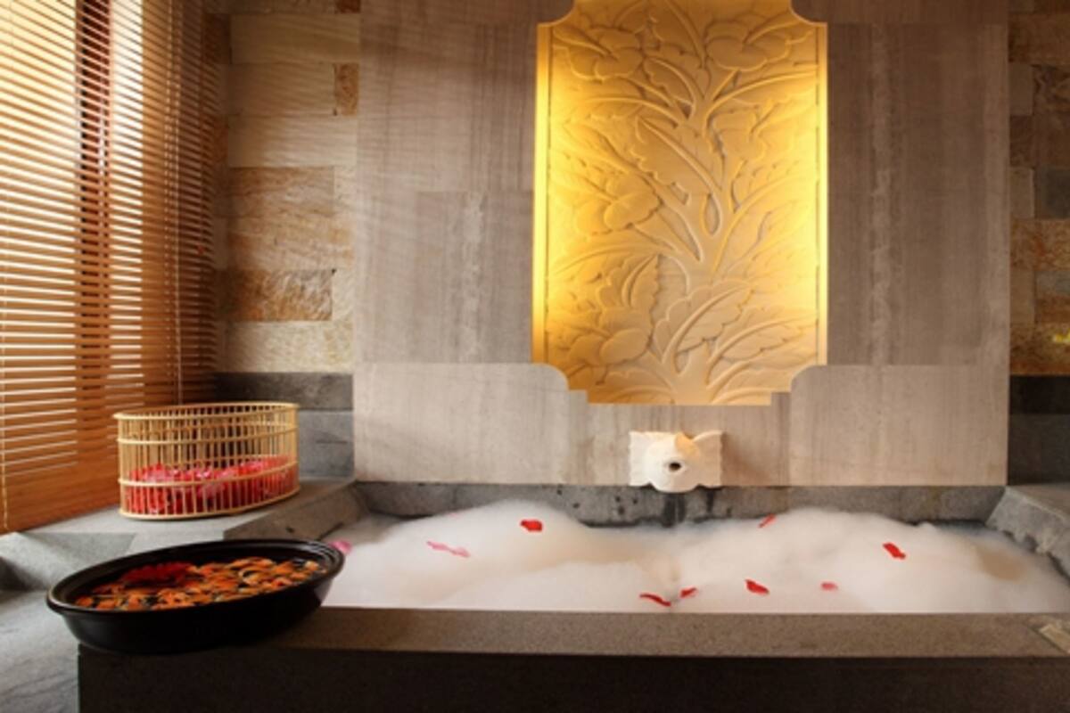 Un área de spa con una bañera de hidromasaje, un muro decorativo, toallas, velas y flores.