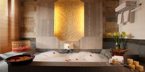 A spa area with a hot tub, decorative wall, towels, candles, and flowers.