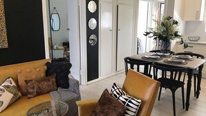 A modern living room with a sofa, a dining table set for four, and a kitchen area visible through an open door.