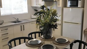 A modern kitchen with white cabinets, a built-in microwave, and a refrigerator. There is a dining table with black chairs and a vase with flowers.