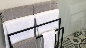 A bathroom with a towel rack holding multiple towels, a patterned floor, and a glass shower door.