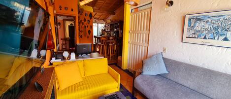 A living room with a yellow sofa, a grey sofa, a television, and a wall-mounted light fixture.