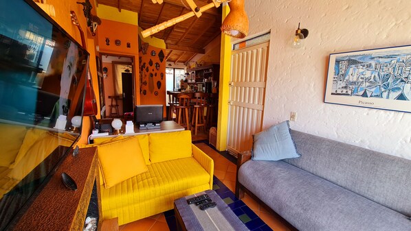 A living room with a yellow sofa, a grey sofa, a television, and a wall-mounted light fixture.