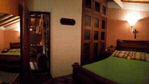 Een kamer met weinig licht, een houten bed, een spiegel en een kledingkast van hout.