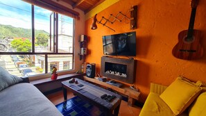 A room with a large window, a television, a guitar, and a fireplace.