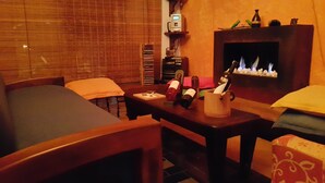 Een gezellige woonkamer met een open haard, een tafel met wijnflessen en een stapel boeken.