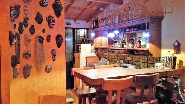 Een restaurant met een bar, houten tafels en stoelen. Op de barplanken staan verschillende flessen en glazen.