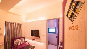 Un salón moderno con un sofá rosa, un televisor y una mesita. Se ve una puerta de madera con una obra de arte y una escalera que lleva a otra habitación.