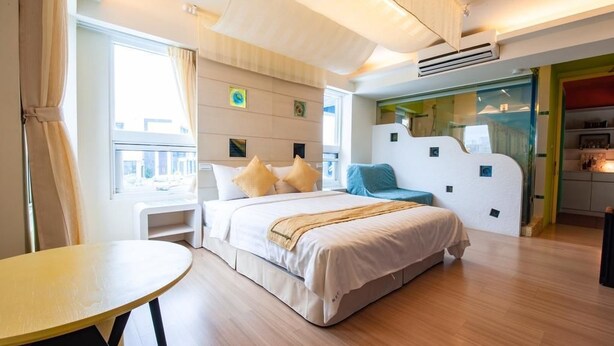 A modern hotel room with a large bed, a small table, and a view of the city through the window. - Indigo Homestay (Magong)